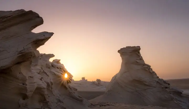 Morning sun flare breaking through natural sand rock formations at Al Wathba Fossil Dunes in Abu Dhabi.