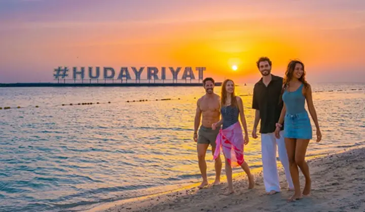 Group of friends strolling along the shoreline of Hudayriyat Beach during a golden sunrise in Abu Dhabi.