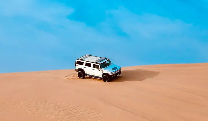 White Hummer H2 driving along the ridge of a vast sand dune during a Hummer desert safari in Abu Dhabi.