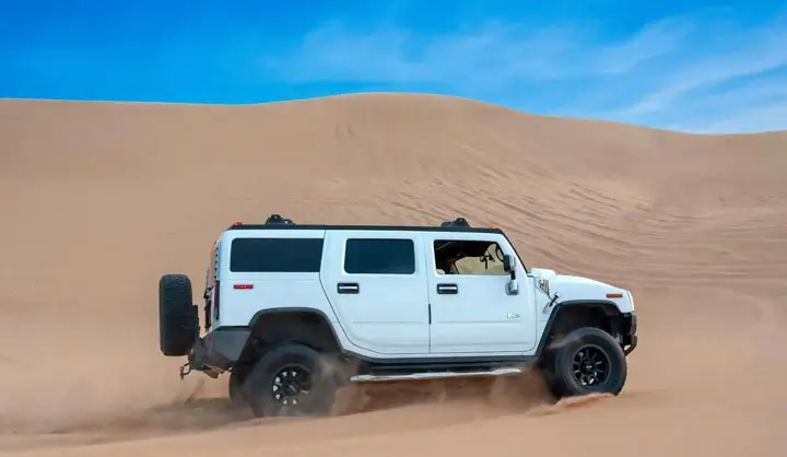 White Hummer H2 kicking up sand while dune bashing through the desert dunes in Abu Dhabi.