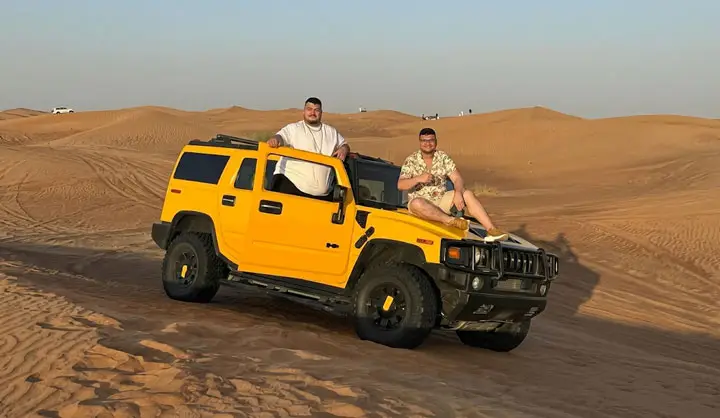 Two men posing with a bright yellow Hummer H2 on the sand dunes during a desert tour in Abu Dhabi.