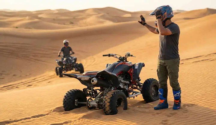 Rider adjusting helmet next to ATV stucked in the sand in Abu Dhabi desert dunes.