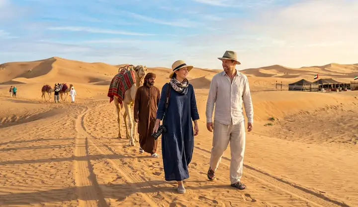Couple walks with a camel and local guide along a sandy track in the Abu Dhabi desert.