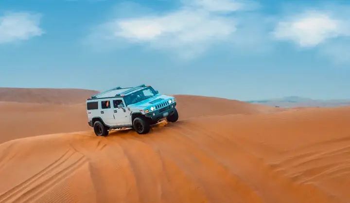 White Hummer H2 navigating orange sand dunes during a Hummer desert safari in Abu Dhabi.