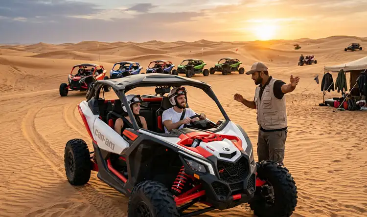 A professional tour guide standing on the sand and giving instructions to a young couple seated inside a white and red Can-Am buggy, with more buggies lined up behind them.