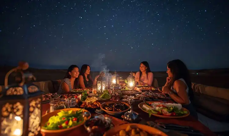 Four women enjoying a lantern-lit gourmet dinner under the starry night sky during an overnight desert safari in Abu Dhabi.